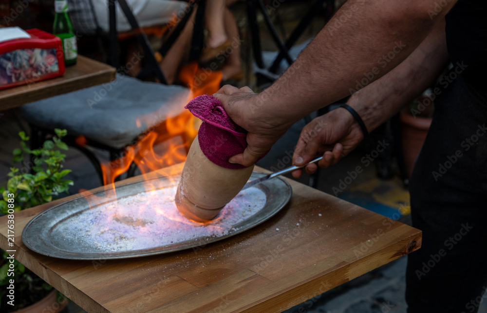 Fototapeta premium Istanbul,turkey,august 2, 2025. Chef dramatically opening a flaming testi kebab clay pot on a heated salt tray in a turkish restaurant, culinary performance