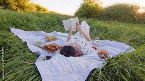 Woman Enjoying a Picnic While Reading a Book in a Green Field