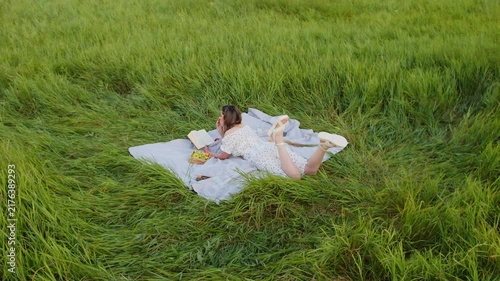 A young woman reads on a blanket in a green field, surrounded by wildflowers