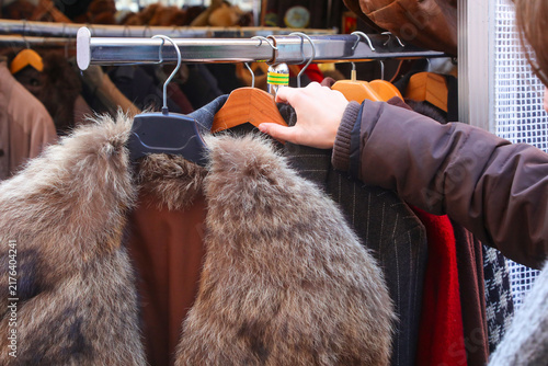 Hand of a customer browsing vintage clothes and fur coat on a rack at an outdoor street market