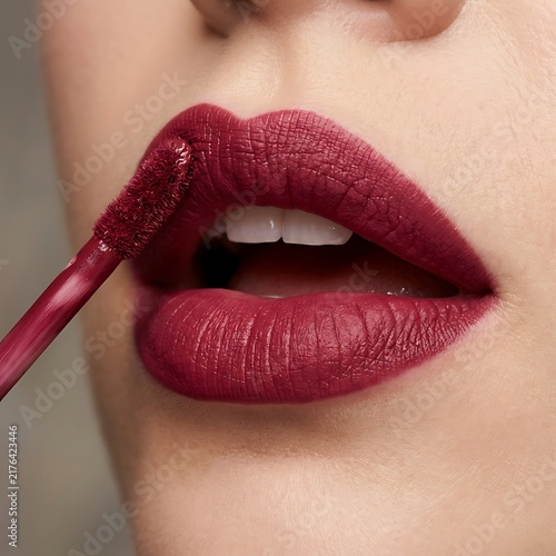 Close up view of a woman applying dark red liquid lipstick
