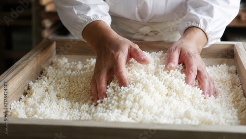 Hands Mixing Rice Koji in Wooden Tray During Traditional Fermentation Process