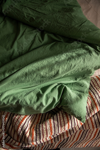 An unassembled bed in the bedroom, a blanket, and green and beige bedding.