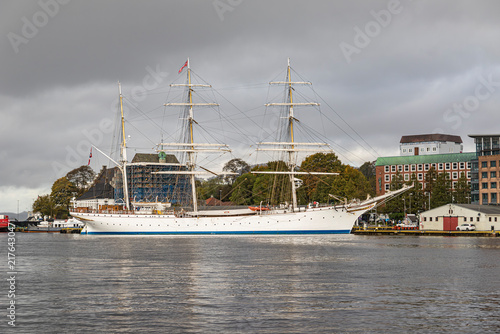 Bild auf Leinwand White historic three-masted tall sailing ship anchored in harbor against cloudy