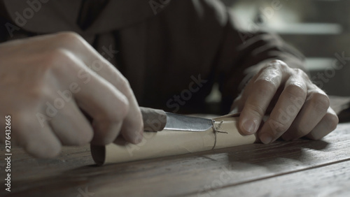 Cuadro en lienzo Medieval monk hands cutting a cord knot on a rolled parchment with a penknife on