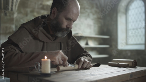 Fotografía Medieval monk cutting a twine string on a parchment paper scroll with a knife at