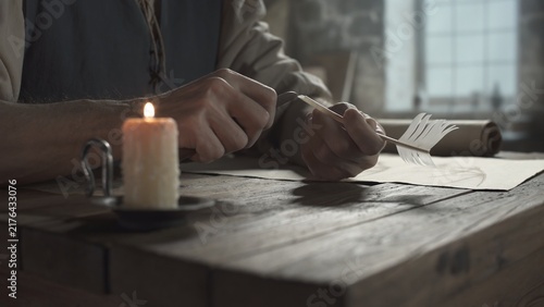 Fotografía Hands of a master sharpening a white quill with a small knife on a rustic table
