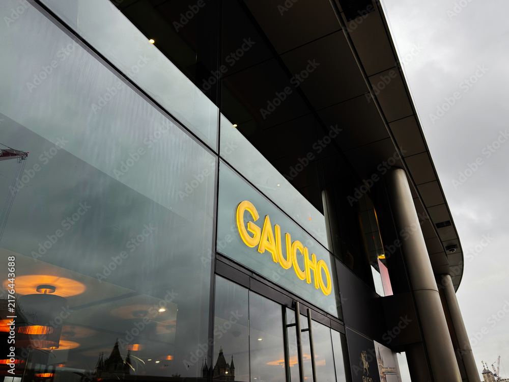 Obraz premium Gaucho restaurant entrance in modern glass facade on the riverside in London, UK with illuminated sign and contemporary architecture