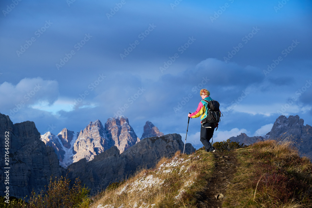 Obraz premium Solo female trekker reaches scenic ridge beneath dramatic storm clouds in Dolomites, Italy, symbolizing achievement, resilience, freedom, remote exploration and connection with wild alpine nature.