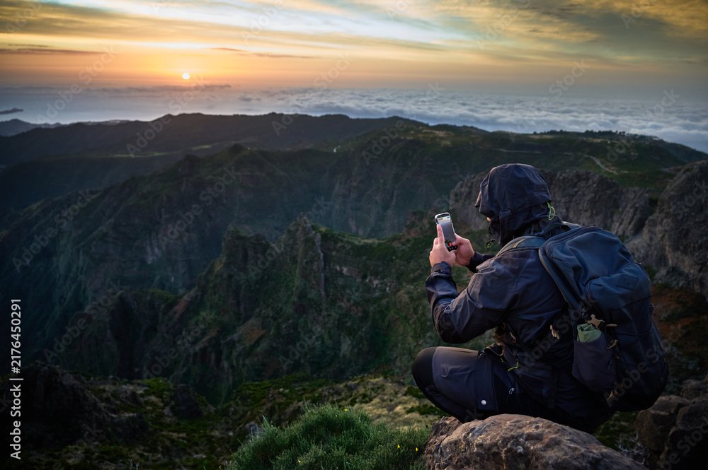 Obraz premium Backpacker films sunrise from Pico do Arieiro rocks, overlooking cloud sea, rugged peaks, valley cliffs, adventure travel and mountain content creation