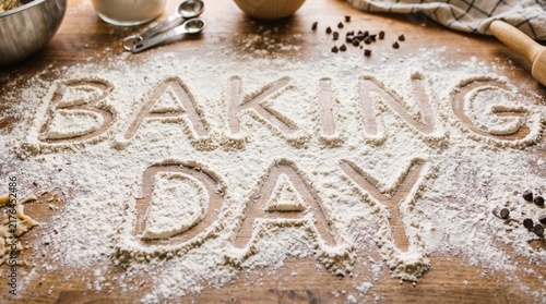 Baking Day flour inscription banner with rolling pin, mixing bowl and cozy kitchen atmosphere
