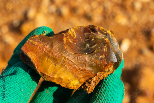 Fotografía Raw brown flint stone held in a worker's gloved hand against a blurred desert qu