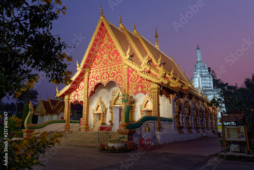 Wat Suan Tan temple beautifully illuminated at night, showing the golden assembly hall and the tall white chedi spire in the background.