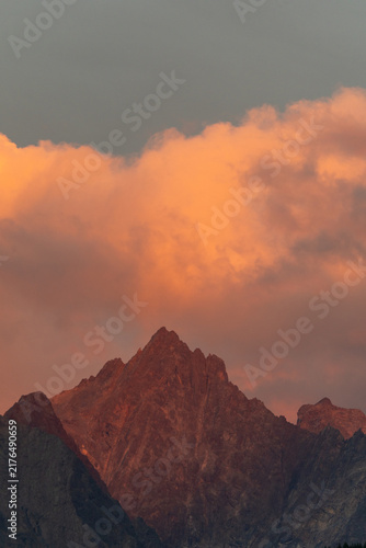 Sunset Alpenglow on Rugged Mountain Peak With Dramatic Orange Clouds and Dusky Sky