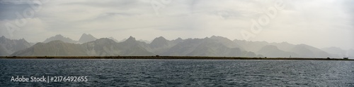 Panoramic Coastal Mountains Over Calm Sea With Moody Sky and Distant Peaks