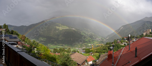 Panoramic Mountain Village Valley With Double Rainbow Over Alpine Landscape And Red Roooftops