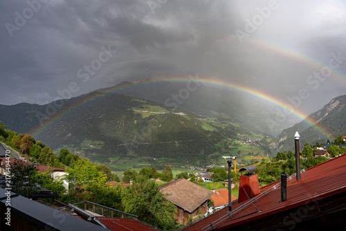 Double Rainbow Over Alpine Village and Lush Mountain Valley With Red Rooftops and Dramatic Sky