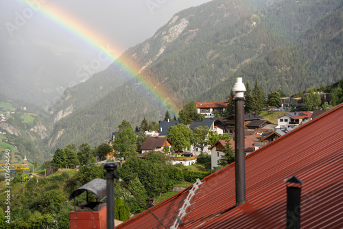 Rainbow Over Alpine Village With Red Rooftops and Forested Mountain Landscape