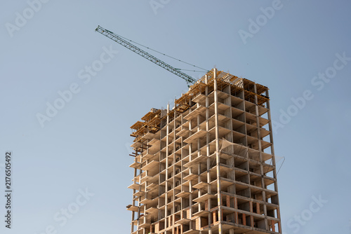 Modern apartment building under construction with green crane under clear sky