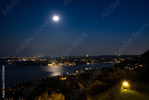 Moonlit night over Lake Garda, Italy and city with reflections and distant lights