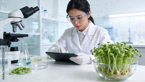 Asian female scientist studying plant growth with microscope and tablet in a modern lab