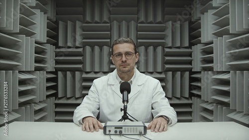Male scientist in lab coat in an anechoic chamber with microphone and scientific equipment