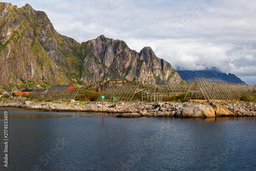 Traditionelle Holzgestelle zum Trocknen von Stockfisch an der felsigen Küste vor einer gewaltigen Bergkette, Svolvær, Norwegen, Europa