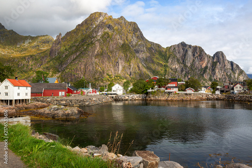 Idyllische Meeresbucht im Fischerdorf vor einer gewaltigen, steilen Felswand mit traditionellen skandinavischen Wohnhäusern, Henningsvær, Norwegen, Europa