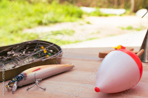 Photography Fishing gear spread out on a wooden surface, including a colorful lure, a sinker, a float and a box of hooks, preparing for a relaxing day of fishing