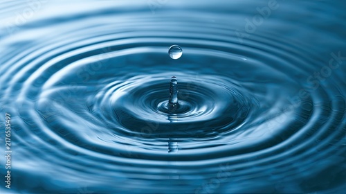 A single water droplet creates expanding concentric ripples on a deep blue liquid surface