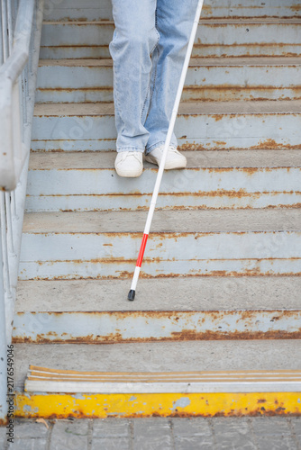 A blind woman descends a staircase. Close-up of her feet and a tactile stick.