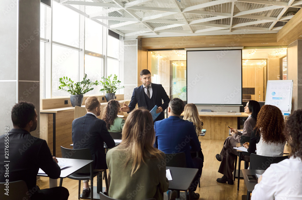 Obraz premium Businesspeople team at training seminar with coach. In a modern office, the coach leads a presentation by a screen as a group attends the meeting. Concept image of corporate training.