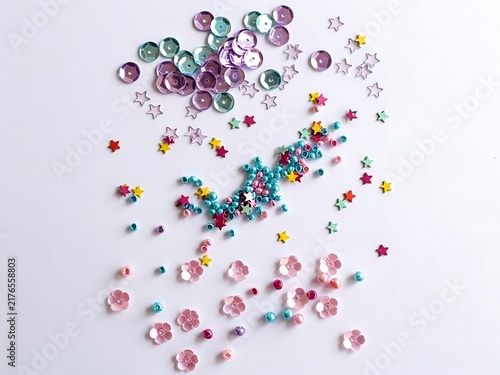 Colorful craft supplies including round sequins star confetti and small beads scattered on white surface