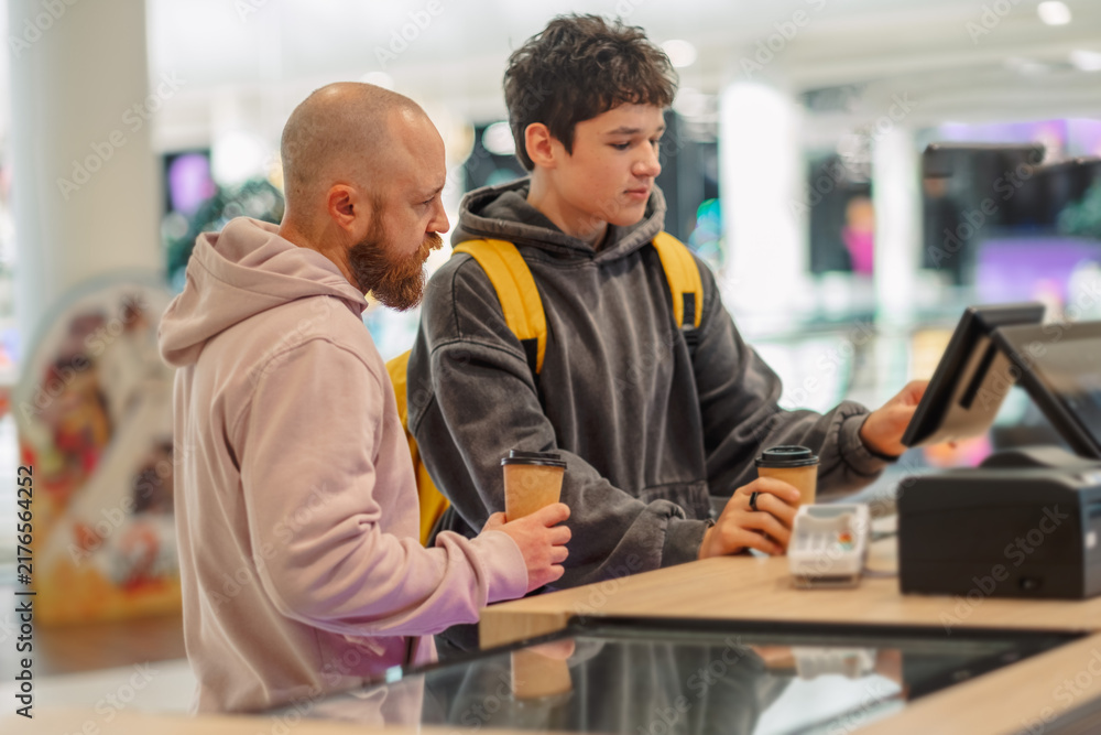 Fototapeta premium Man and teenage boy at a cafe counter with a touchscreen