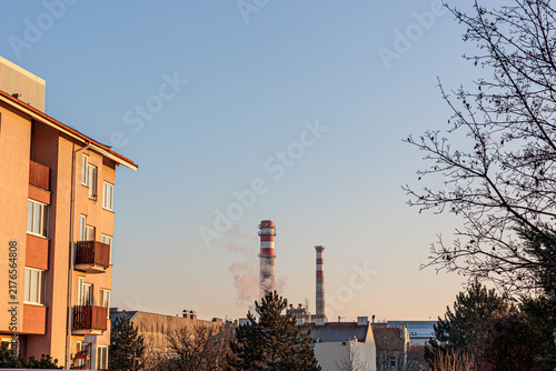 Canvastavla Apartment Building and Industrial Smokestacks at Sunset With Bare Trees in Urban