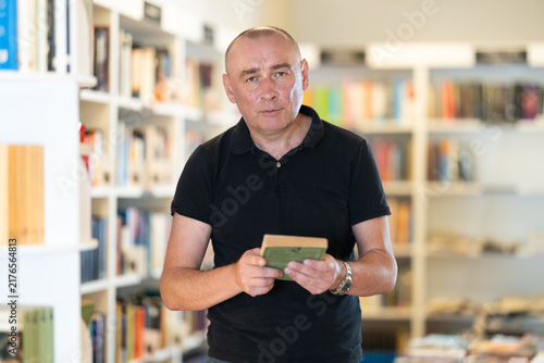 Obraz na plátně Adult male reader explores aisles of bookstore, looking for new title to enjoy