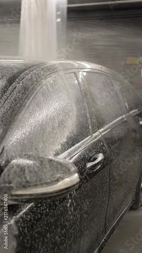 Black luxury car covered in white soap suds during a professional car wash. Car wash concept.