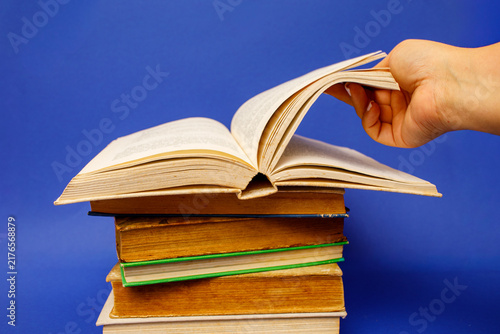 Cuadro en lienzo A hand flips the pages of an open book resting on a stack of closed hardcover bo