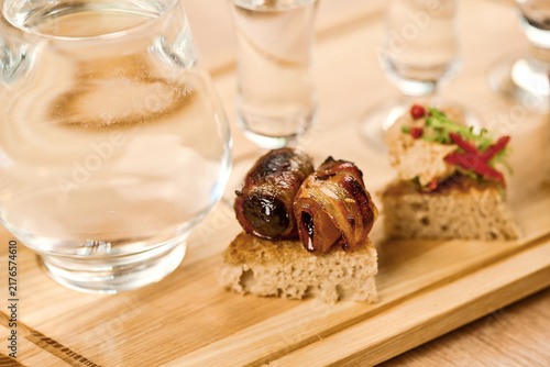 Appetizing platter with meat, bread, and shot glasses on wooden board