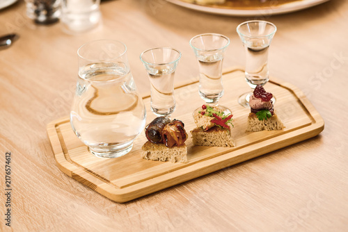 Assorted appetizers with shots of liquor on wooden serving board