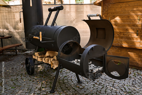 Black metal smoker grill with wood storage on cobblestone patio
