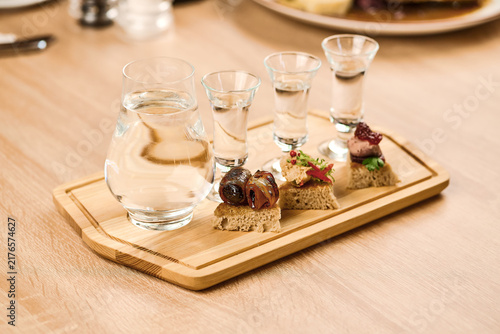 Assorted appetizers with shot glasses and water on wooden serving board