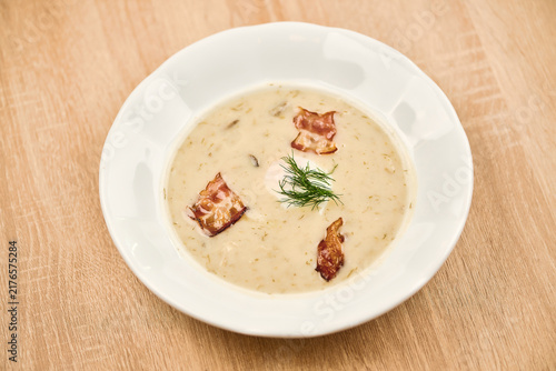 Creamy soup with crispy bacon and dill garnish in white bowl