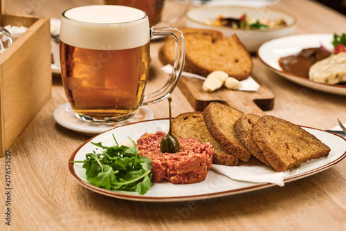 Plate of beef tartare with toasted bread and beer on wooden table