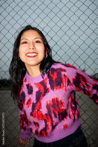 Dynamic low angle portrait of a smiling young latina woman in a colorful sweater outdoors