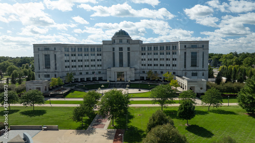 Aerial view of the Michigan Supreme Court building surrounded by lush green trees, manicured lawns, and American and state flags flying in Lansing, Michigan, United States.