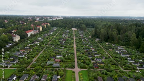 aerial drone video of Kumpula Allotment Gardens in Helsinki, Finland, surrounded by lush green vegetation, garden plots, small cottages, and peaceful summer scenery.