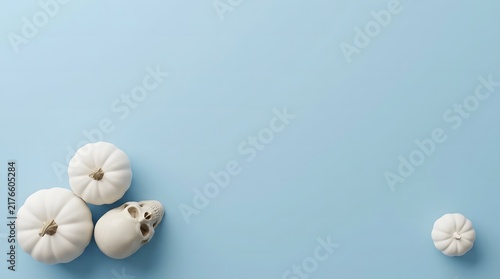 Minimalist halloween background with small white pumpkins and a skull on a light blue surface