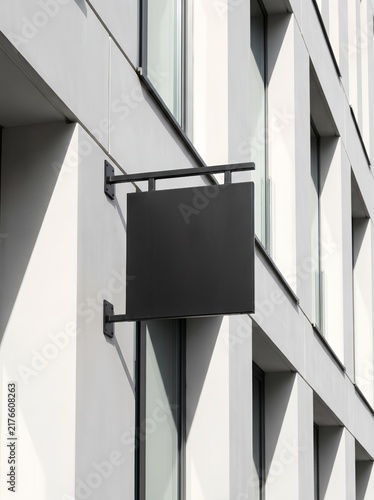 Empty matte black square sign with metal brackets on clean white architectural facade, mockup space
