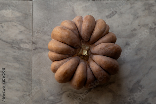 Whole pumpkin placed on a white and grey marble floor.